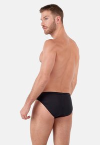 Bañadores negros con un diseño de tiro bajo, textura suave y corte minimalista, que presentan una cintura discreta y sin marca visible.
