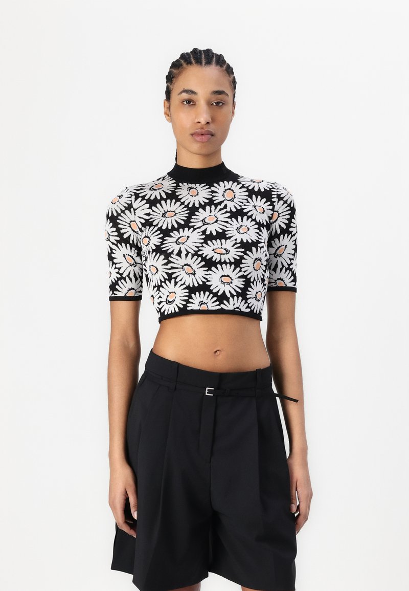 Svart avskåret topp med hvit tusenfryd mønster og oransje senter, tettsittende design med korte ermer, brukt med høyt liv svarte shorts.