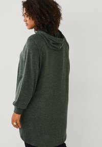 Langsleeve, donkergroen hoodiejurk van een zachte, gestructureerde stof. Heeft een capuchon en een relaxte pasvorm, met ribbelboorden en een afgeronde zoom.
