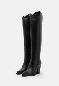 Botas de cuero negro hasta la rodilla con punta afilada, tacón bloque y borde superior ondulado. Textura suave con un detalle mínimo.