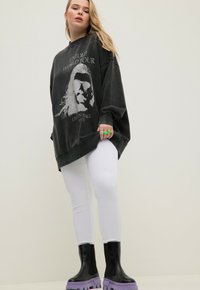 Överdimensionerad svart sweatshirt med grafiskt tryck, vita ribbade leggings och ankelboots med en tjock lila sula. Grön ringdetalj.