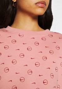 Rosa sweatshirt med ett mönster av Nike-logotyper och cirkulära grafiker. Mjuk textur och ribbad krage.