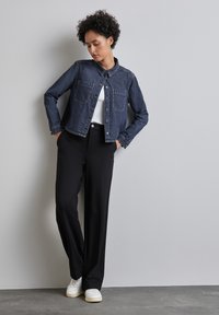 Jeansjacka med krage, två bröstfickor och knappstängning, parat med svarta vida byxor och vita sneakers.