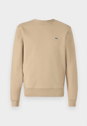 Beige sweatshirt with round neckline, long sleeves, ribbed cuffs and hem. Features a small green crocodile logo on the chest. Smooth texture.