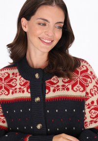 Sweter zapinany na guziki w granatowym wełnianym kolorze z wzorem Fair Isle w odcieniach czerwieni i kremu. Posiada prążkowany kołnierz i mankiety oraz cztery guziki w złotym odcieniu.