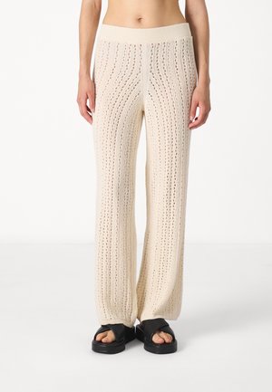 Gestrickte cremefarbene weite Hosen mit vertikalen Streifenmustern und offenen Details. Sie verfügen über einen weichen, gerippten Bund für zusätzlichen Komfort.