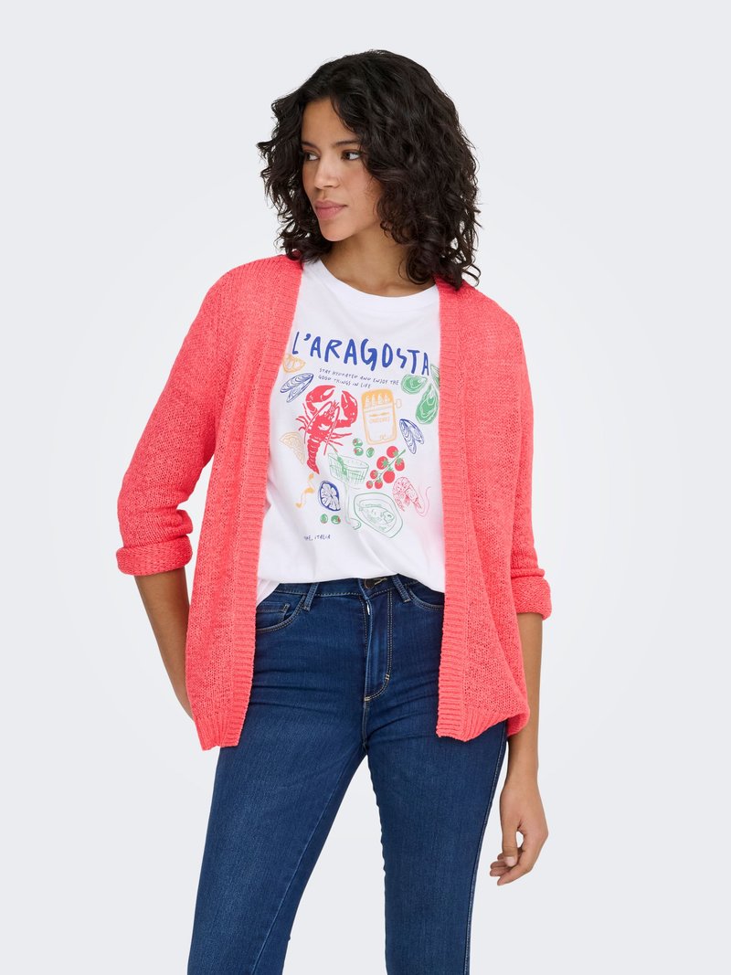 Coral knit cardigan with open front and three-quarter sleeves, paired with a white graphic T-shirt and dark blue skinny jeans.