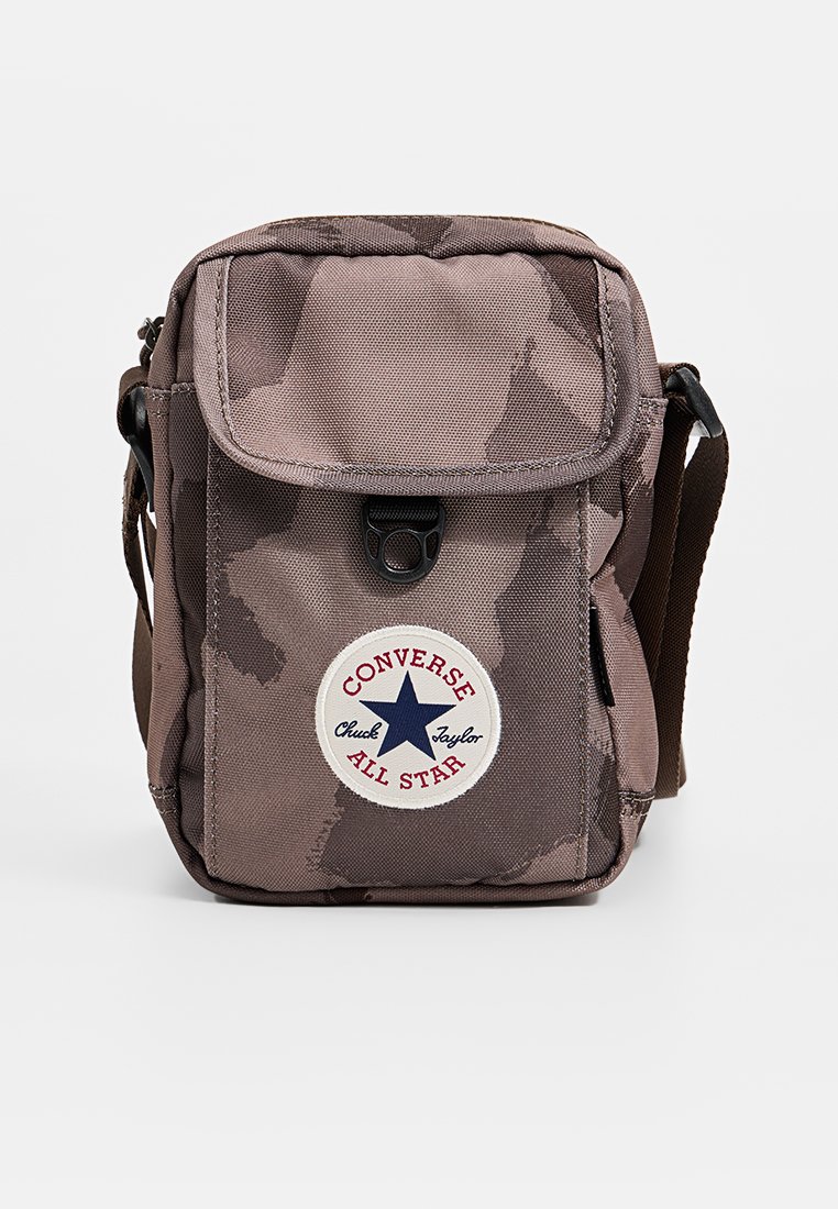 Bruine camouflageschoudertas met een klapflap, een drukknoopsluiting en een cirkelvormig Converse-logo met een blauwe ster. Inclusief een verstelbare band.