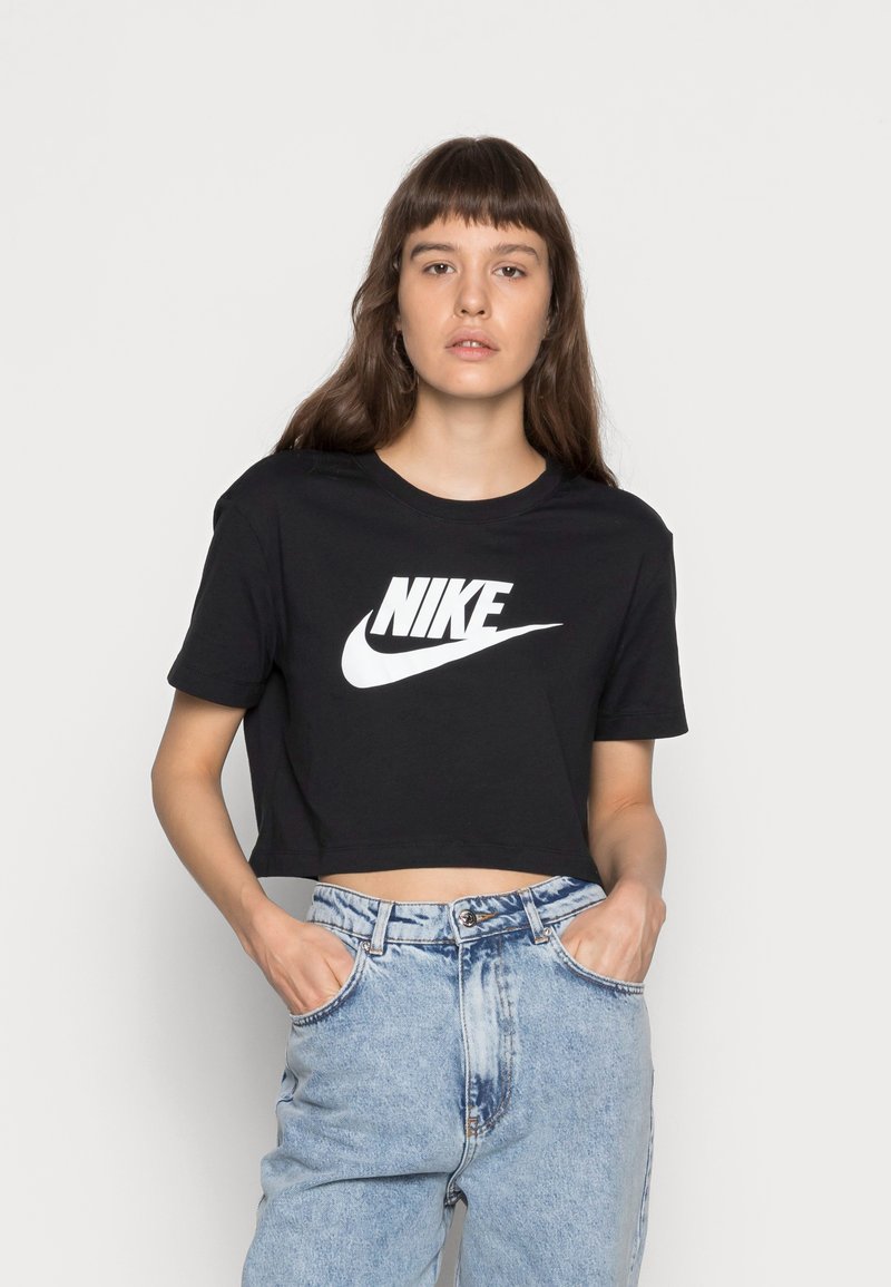 Camiseta negra cortada de algodón con un logo de Nike blanco. Presenta mangas cortas y un cuello redondo. Combinada con unos jeans de mezclilla azul claro.