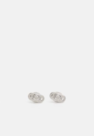Paire de petites boucles d'oreilles clous rondes en ton argenté, avec une base légèrement ovale et une finition lisse et polie sur un fond blanc uni.