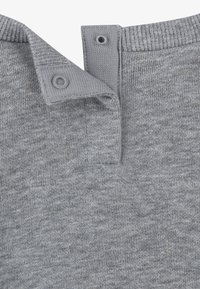 Cuello de suéter de punto gris con tela texturizada, dos cierres a presión en el cuello y bordes acanalados, con un sutil patrón jaspeado.