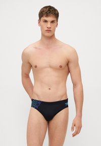 Sorte svømmebriefs med blå og lilla diagonale striper, med en glatt tekstur og en beskjeden skjæring. Logo plassert på siden.