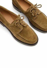 Zapatos de ante marrón con cordones y punta redondeada, con acentos cosidos y suela plana negra. Forro de cuero. Presentan cordones clásicos.