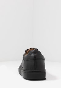 Czarne skórzane sneakersy widziane z tyłu, z grubą podeszwą i subtelnie wytłoczonym nazwiskiem marki na kołnierzu pięty.