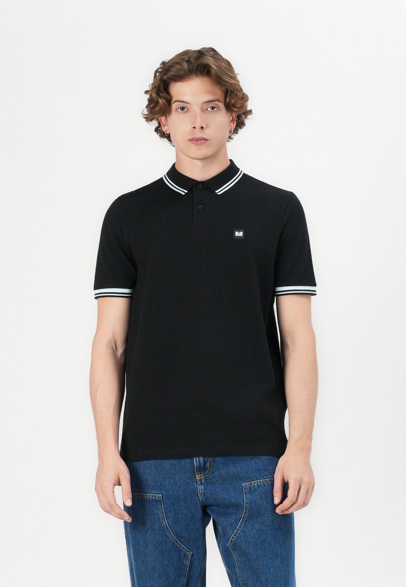 Black polo shirt with short sleeves, contrasting white stripes on the collar and sleeve cuffs, featuring a small logo patch on the chest.