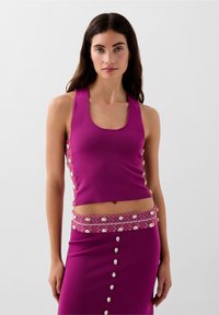 Top a fascia viola aderente con spalline larghe, tessuto testurizzato, caratterizzato da bottoni a conchiglia decorativi lungo i lati e una gonna abbinata con una vita a fantasia.