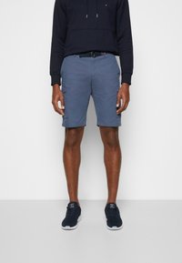 Graue Cargo-Shorts aus leichtem Stoff, mit Taschen und einem Gürtel. Getragen mit einem marineblauen Sweatshirt und marineblauen Sneakern.
