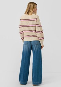 Beżowy sweter z dzianiny w różowe i brązowe paski, zestawiony z wysokim stanem szerokimi niebieskimi dżinsami o wypłowiałym wykończeniu i przeszyciami.
