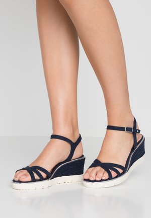 Granatowe sandały na koturnie z wieloma paskami, teksturowanym, plecionym koturnem i białą gumową podeszwą. Pasek wokół kostki z regulowaną sprzączką.