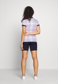 Vit och marinrutig polo med röda detaljer, matchad med marinblå shorts. Kortsleeves, stickad krage och en figurnära design.