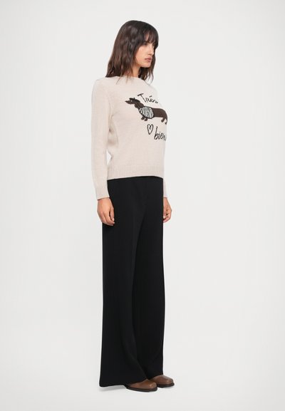 Beige sweater with a dachshund graphic and text, paired with black wide-leg pants. Textured fabric. Brown flat shoes. Simple design.