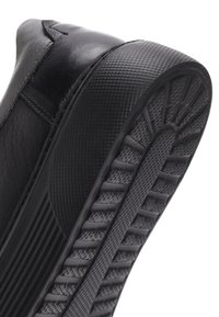 Zapatilla negra con parte superior de cuero texturizado, suela de goma con un agarre patternado y diseño de punta redondeada.