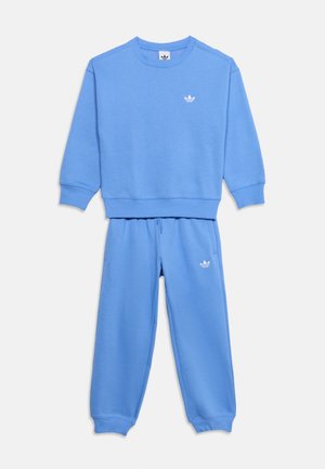Ανοιχτό μπλε φούτερ Adidas με στρογγυλή λαιμόκοψη και ταιριαστό παντελόνι φόρμας με λευκό λογότυπο στο στήθος και στο μηρό, απλωμένα επίπεδα σε λευκό φόντο.