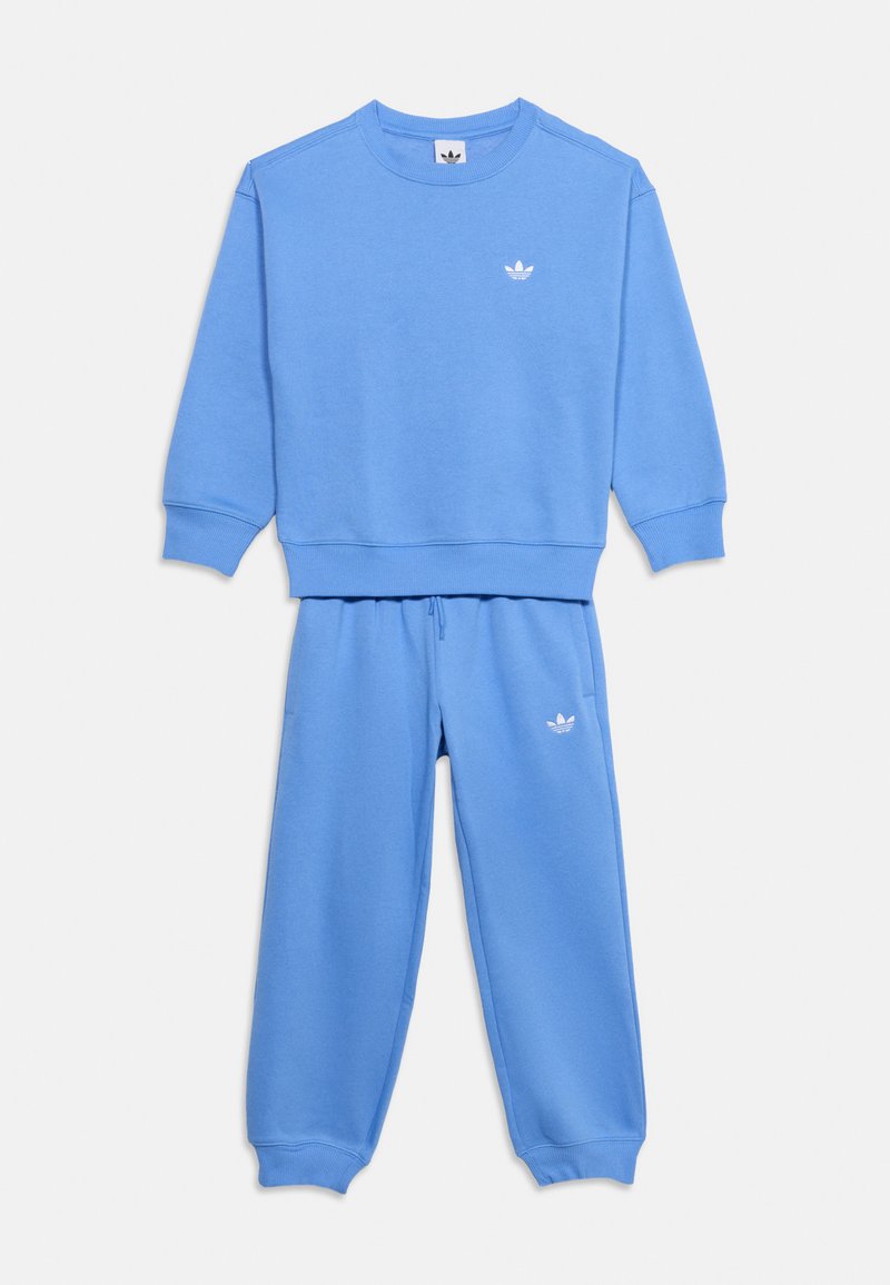 Ανοιχτό μπλε φούτερ Adidas με στρογγυλή λαιμόκοψη και ταιριαστό παντελόνι φόρμας με λευκό λογότυπο στο στήθος και στο μηρό, απλωμένα επίπεδα σε λευκό φόντο.