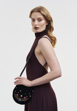 Črna žametna torbica čez ramo s pisanimi cvetličnimi vezeninami, zlatimi zvezdicami in ukrivljeno obliko. Nastavljiv usnjen naramni pas.