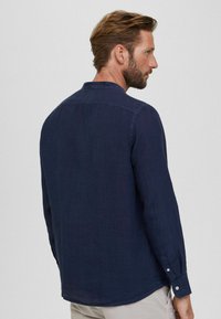 Camicia a maniche lunghe di un blu scuro, realizzata in tessuto leggero, con colletto a punta e polsini abbottonati, e orlo dritto.