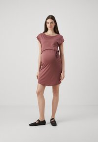 Raseduskleit pehmest mauve kangast, lühikeste varrukatega, ümmarguse kaelusega, külgedelt reguleeritava sidumisega sobivuse tagamiseks, põlvepikkune lõige. Stiilitud mustade lamedate kingadega.
