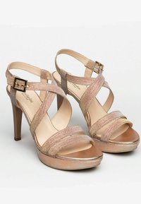 Strappy high-heeled sandals in rose gold, featuring textured straps, a buckle closure, and a platform. Smooth metallic accents on the sole.