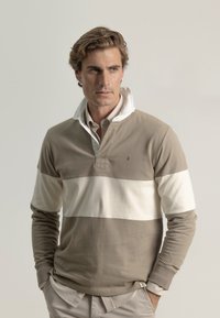 Polo de manga larga en bloques de color beige y crema. Cuenta con un cuello tipo polo, una abertura con botones y una tela suave de textura.