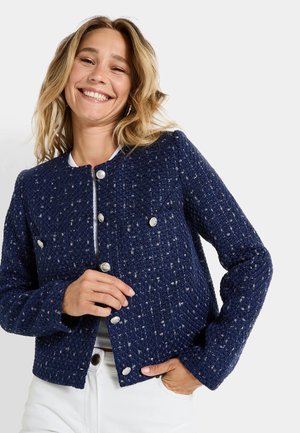 Veste texturée bleu marine en tissu tissé avec des accents métalliques, design ajusté et boutons argentés, dotée d'un col rond.
