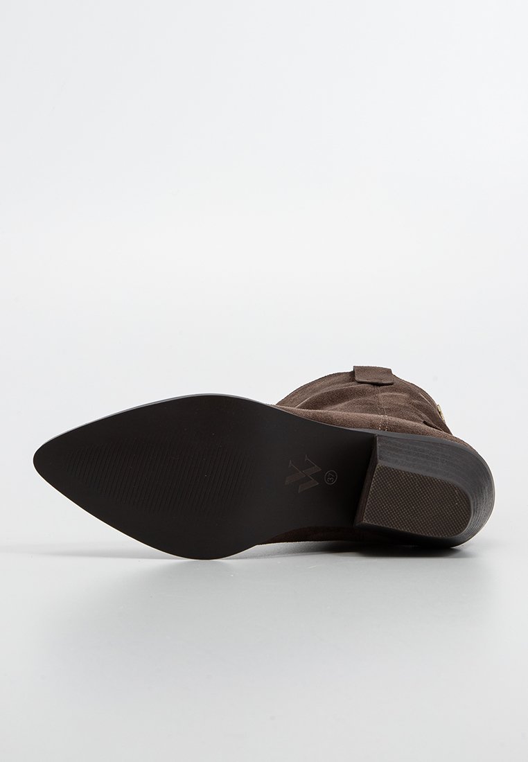 Stivale alla caviglia in suede marrone scuro con punta affusolata, suola testurizzata e tacco modesto. Presenta dettagli hardware e cuciture accentate.