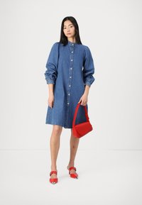 Denim shirt dress with long puff sleeves, front button closure, and a flared hem. Complemented by red handbag and matching red heeled shoes.
