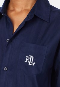 Marineblaues Hemd mit Knopfverschluss aus einem Stoff mit subtiler Textur. Mit einer linken Brusttasche, die mit dem weißen gestickten "RL"-Logo verziert ist.