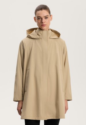 Manteau imperméable beige avec un grand col et une capuche. Présente une silhouette droite et ample ainsi que des poches latérales. Texture lisse et mate.