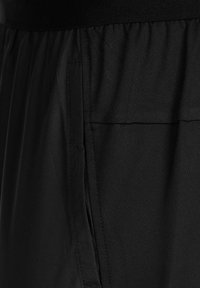 Pantalons de sport noirs avec une texture lisse, une taille élastique et une poche latérale avec des détails brodés.