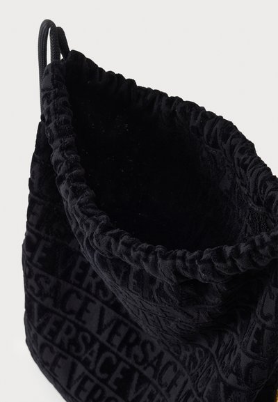 Crna baršunasta torba u obliku kante s naboranim vrhom, ukrašena utisnutim uzorkom logotipa Versace. Mekana tekstura, okrugli oblik i zatvaranje na vezicu.