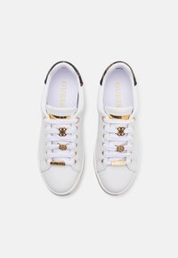 White leather sneakers with gold accents, featuring a patterned black heel, flat white laces, and a golden logo on the tongue.