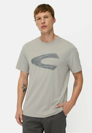 Ung mand med kort brunt hår iført en lysegrå t-shirt med et stort falmet mørkegråt motiv på brystet.
