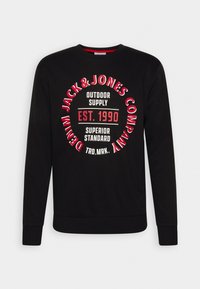 Sweat-shirt noir à manches longues avec un texte circulaire rouge et blanc indiquant « Denim Jack & Jones Company », « Outdoor Supply » et « Est. 1990 Superior Standard ».