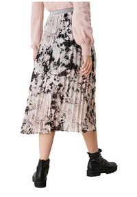 Femme portant des bottes de combat noires et une jupe midi plissée avec un motif marbré rose, noir et blanc ainsi qu'un pull rose.