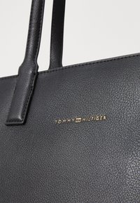 Black leather handbag with a textured finish, featuring two sturdy handles and a gold "TOMMY HILFIGER" logo on the front.