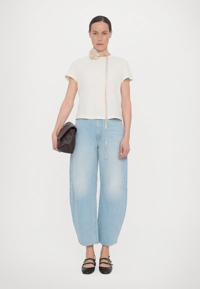 Cream short-sleeve top with a textured flower accent, paired with light blue wide-leg jeans and a dark brown clutch. Black strap shoes.
