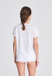 Vit t-shirt med kort ärm i lättviktsmaterial. Avslappnad passform med uppvikta ärmar, som har en subtil textur och en längre bakre fåll.