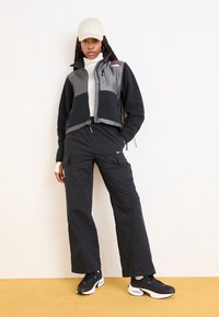 Fleece jacket in black and gray with zip closure, paired with black cargo pants featuring side pockets and logo. Black sneakers with white accents.