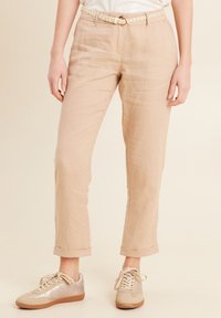 Beige Leinenhose mit geradem Schnitt, umgeschlagenen Bündchen und einem gewebten Gürtel mit einer runden Schnalle; kombiniert mit hellbeigen Sneakers.