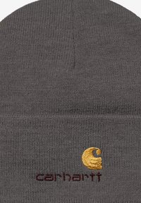 Szary dzianinowy beanie z miękkiego materiału, z podwiniętym brzegiem, z wyraźnym haftem logo Carhartt w kolorach żółtym i burgundowym.